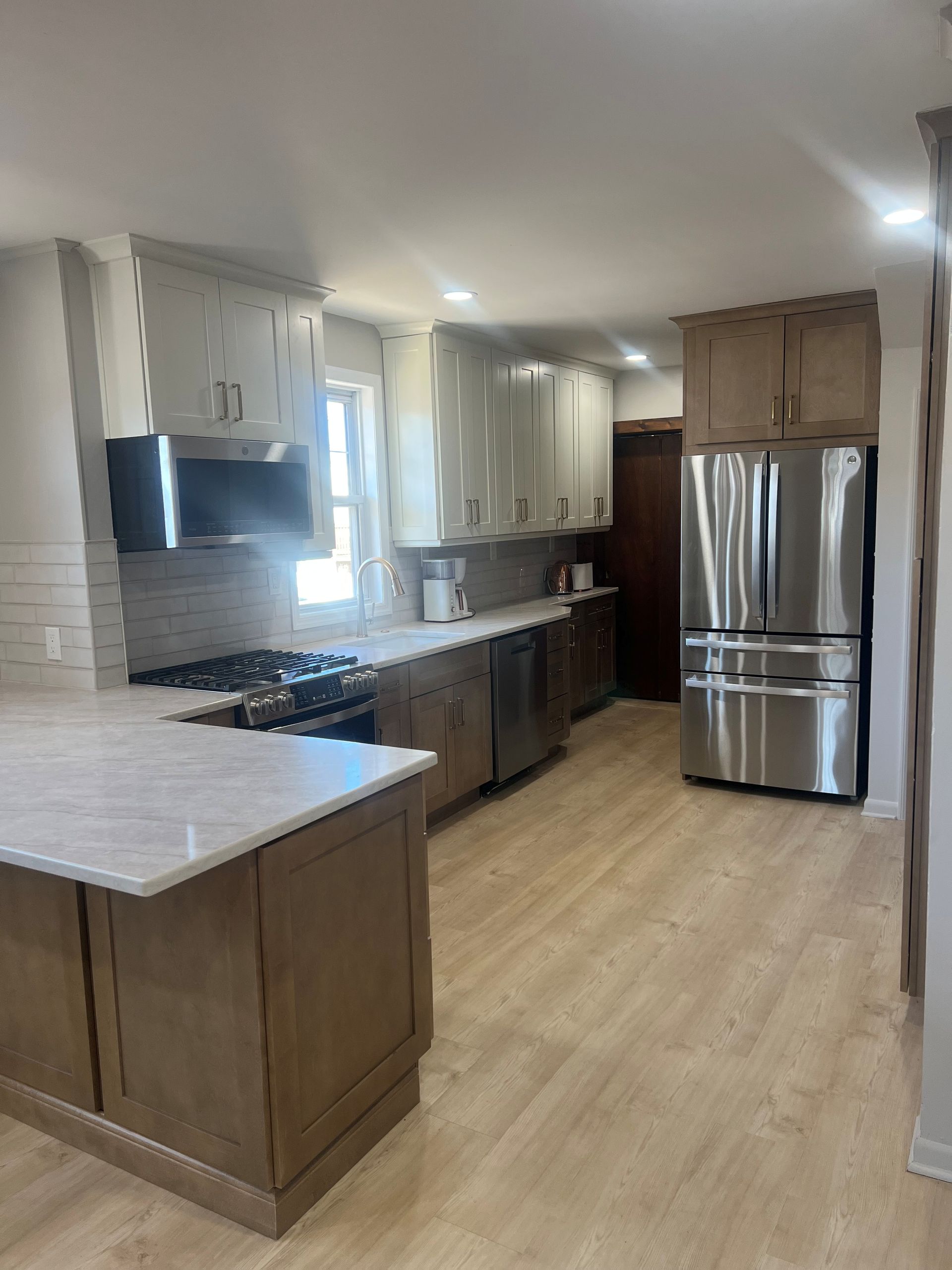 A modern kitchen with white upper cabinets, brown lower cabinets, light countertops, and stainless steel appliances. 