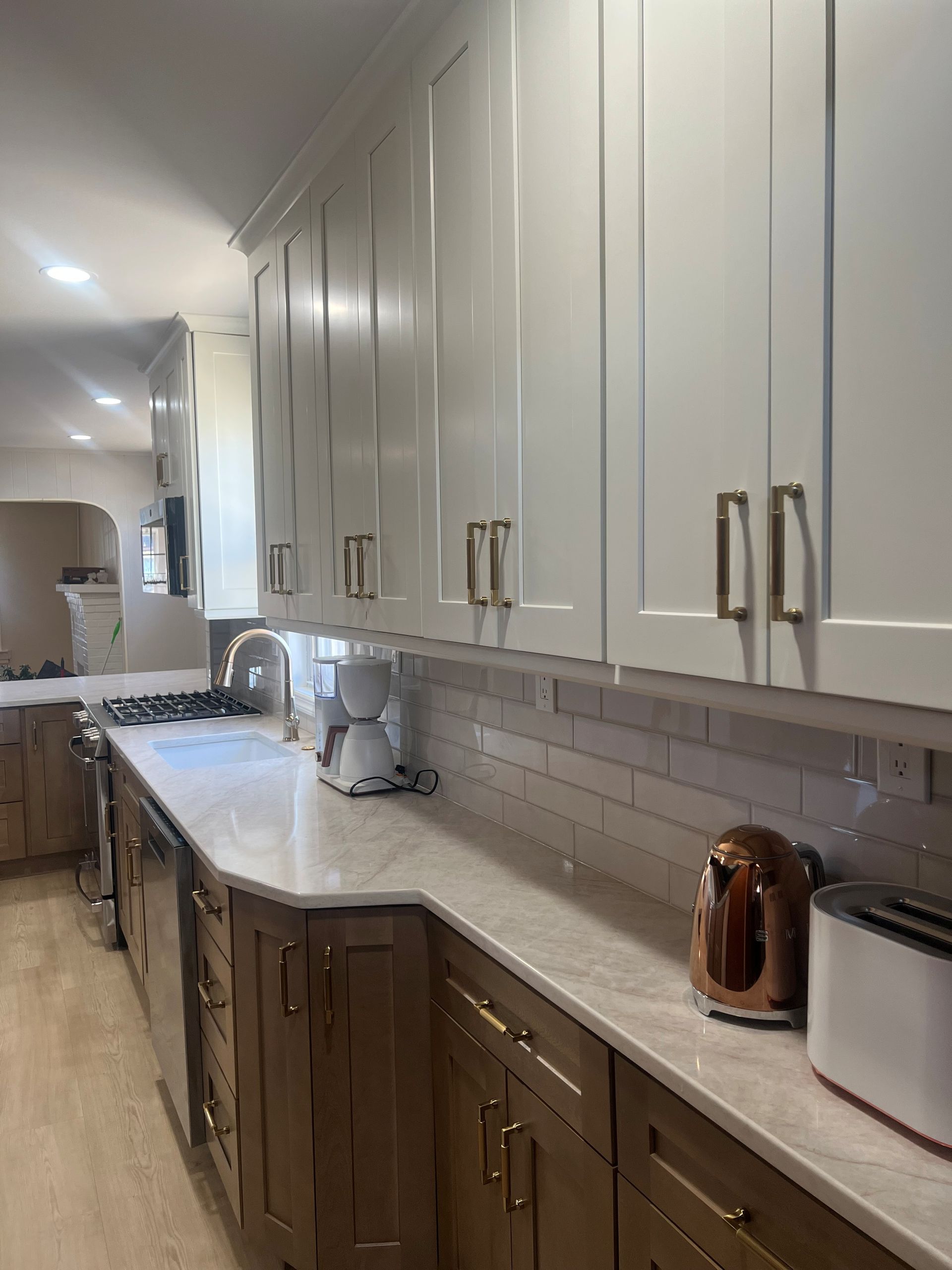 A modern kitchen with upper white cabinets, lower wood-toned cabinets, a marble-patterned countertop, and brass hardware. 