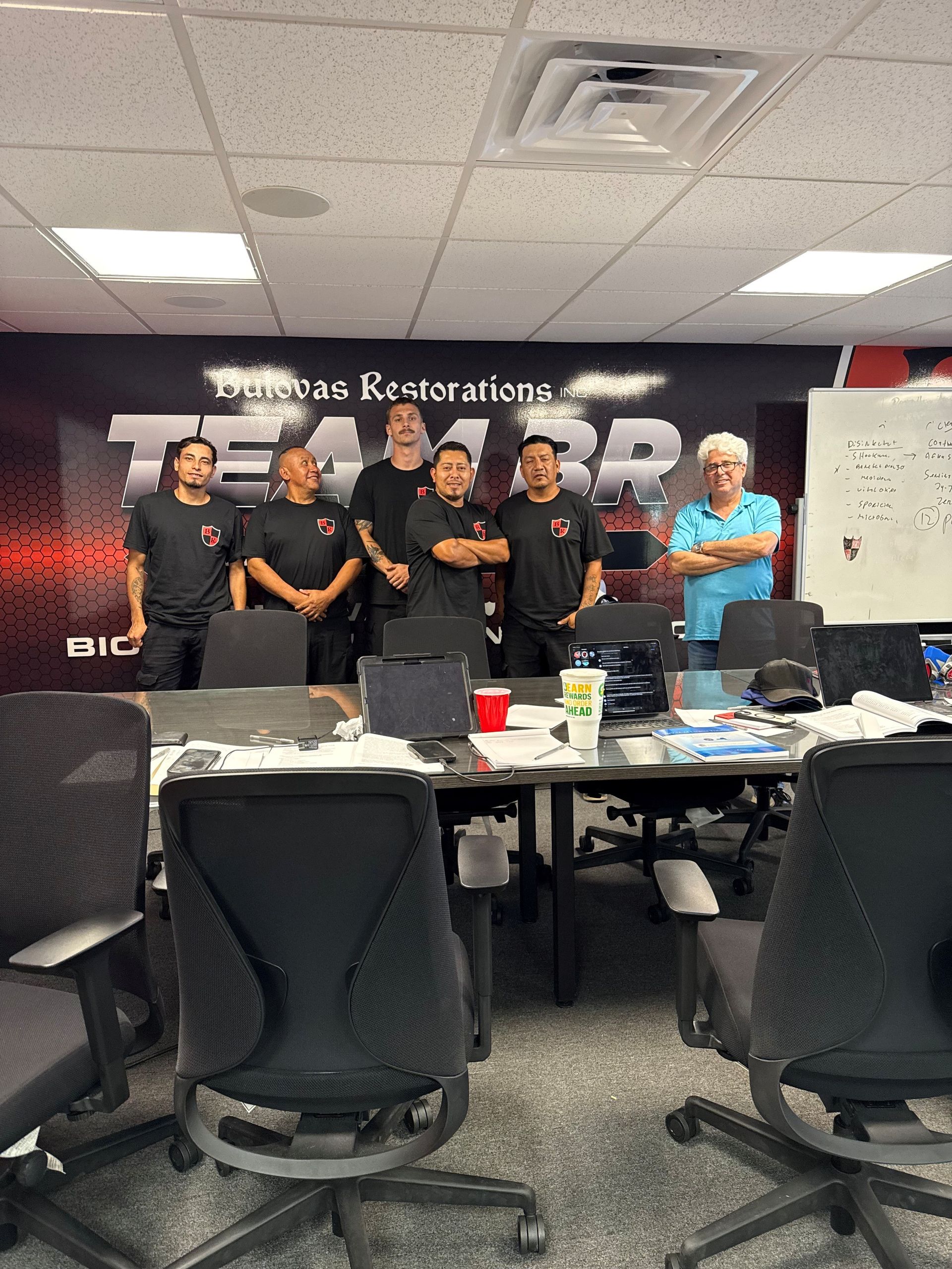 A group of seven people in a conference room, standing behind a table. TEAM ARB logo on the wall.