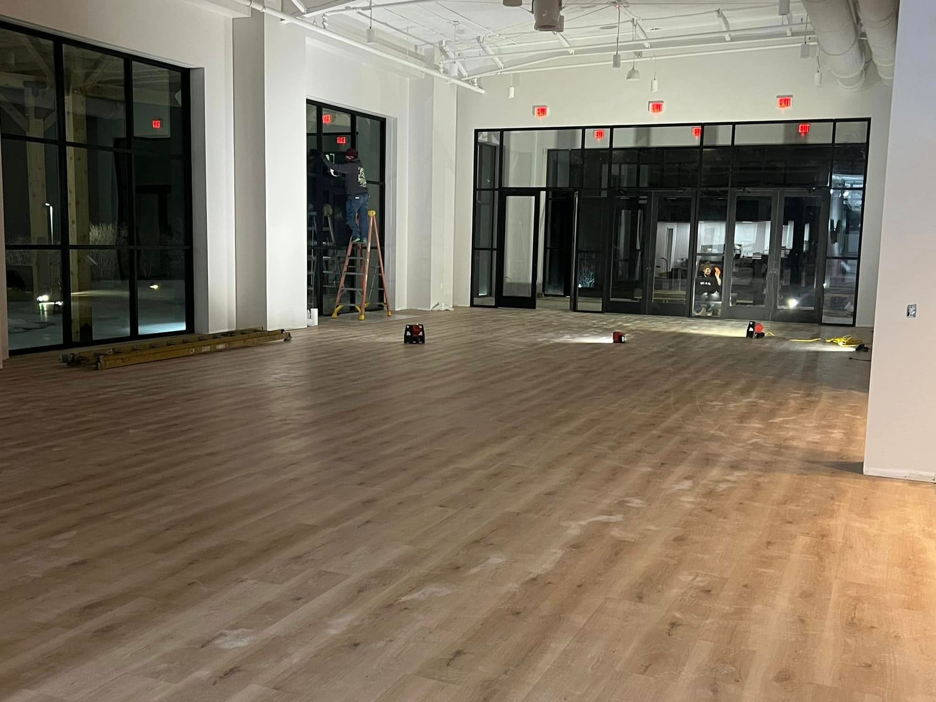 Interior view of a commercial space under construction with large windows and unfinished wooden floors.