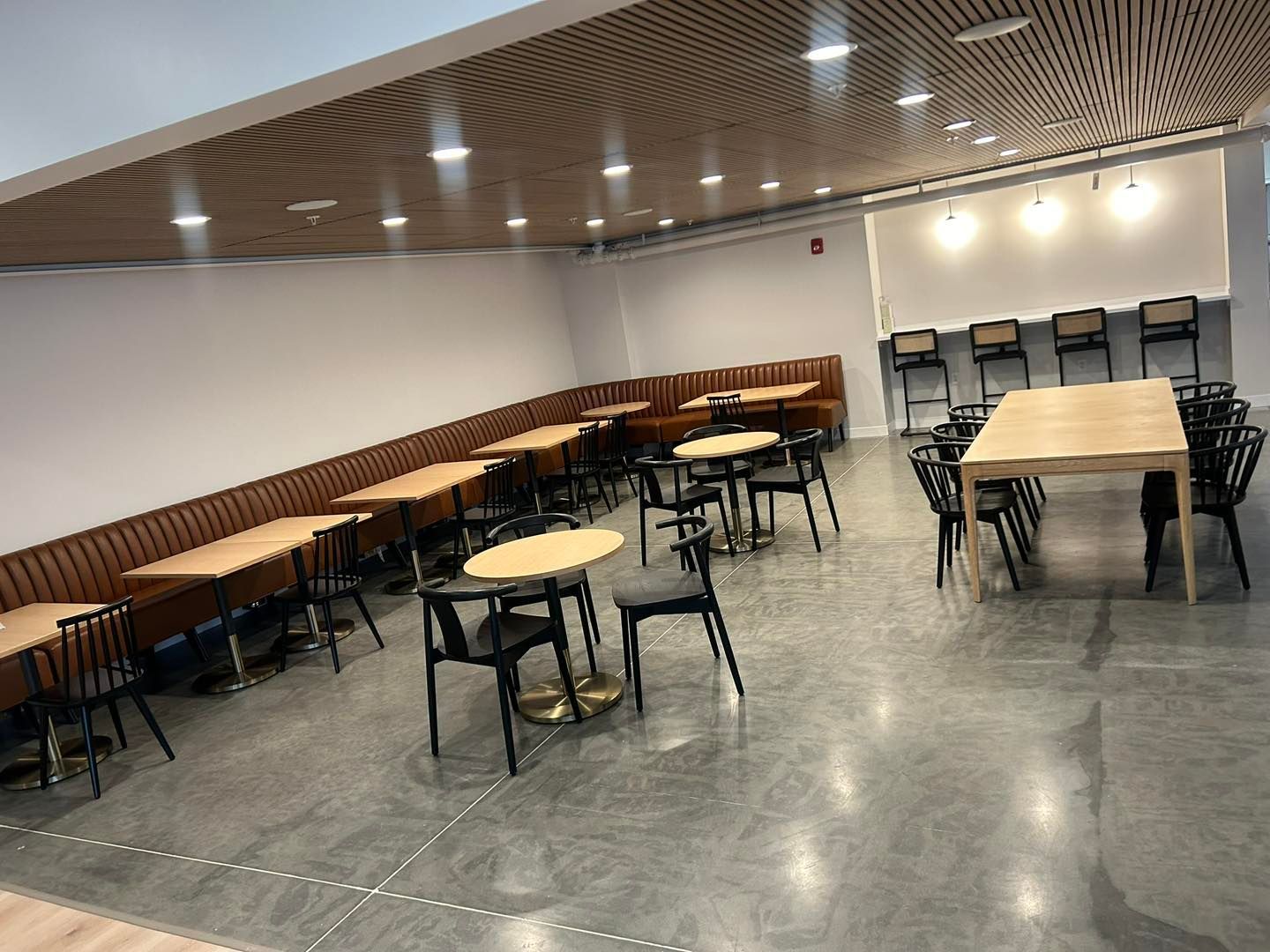 Restaurant interior with tables, chairs, and booths. Wood panel ceiling and gray flooring.