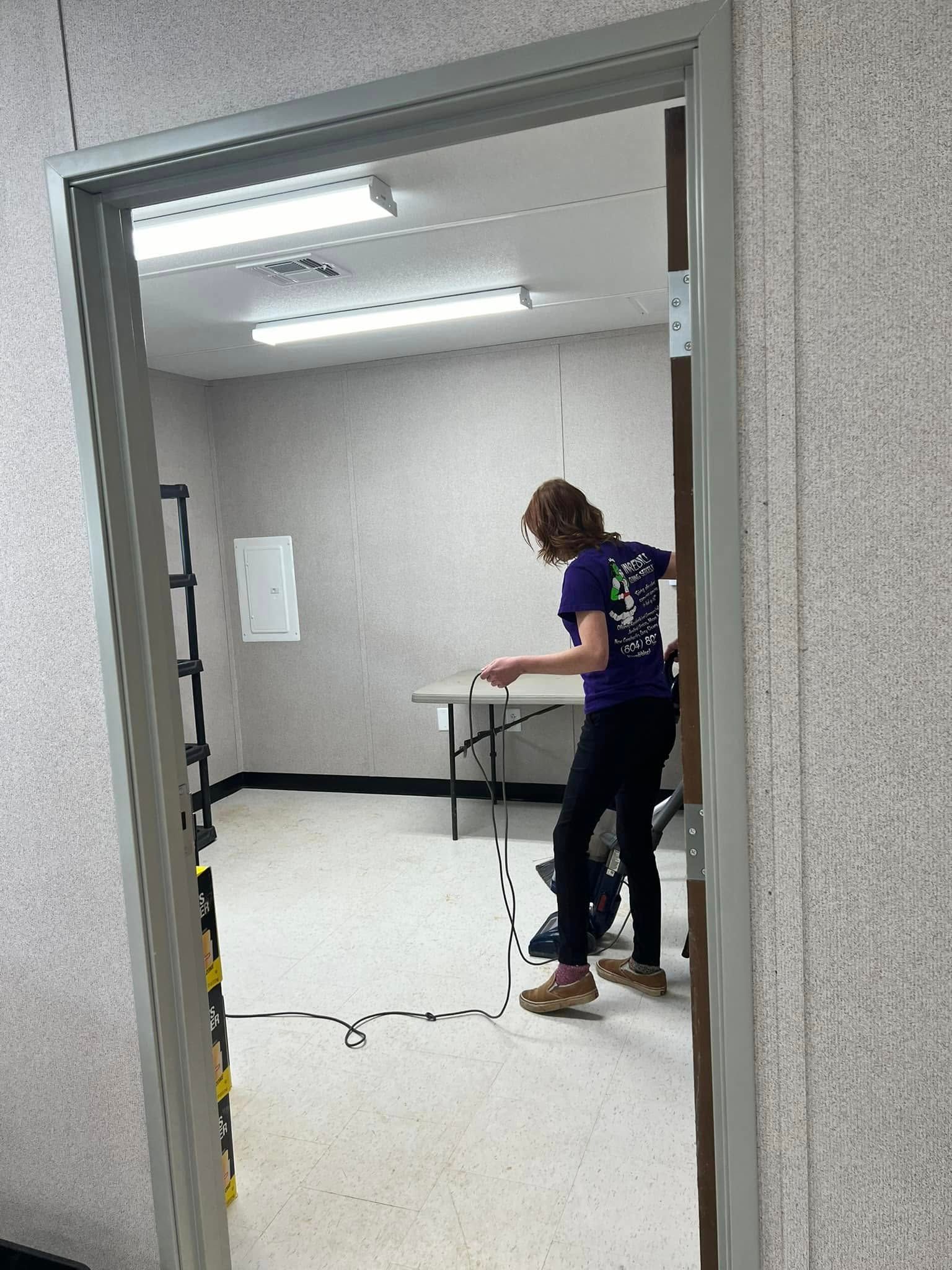 Person in doorway, measuring with a pen in a plain room, folding table in the background.
