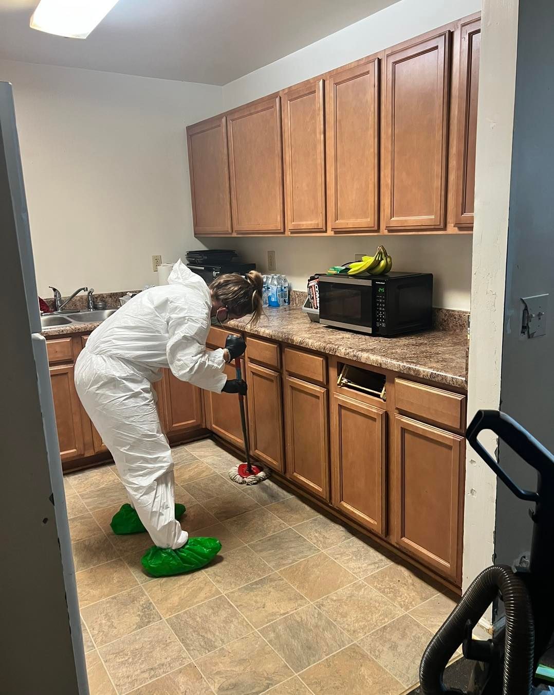 Person in protective suit sprays kitchen floor.