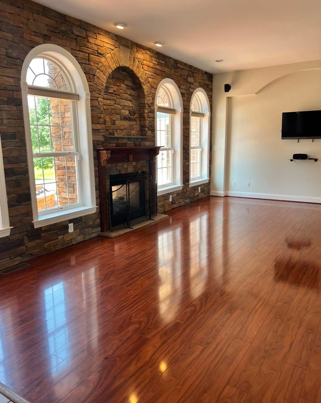 Living room with hardwood floors, a stone accent wall, fireplace, and arched windows.