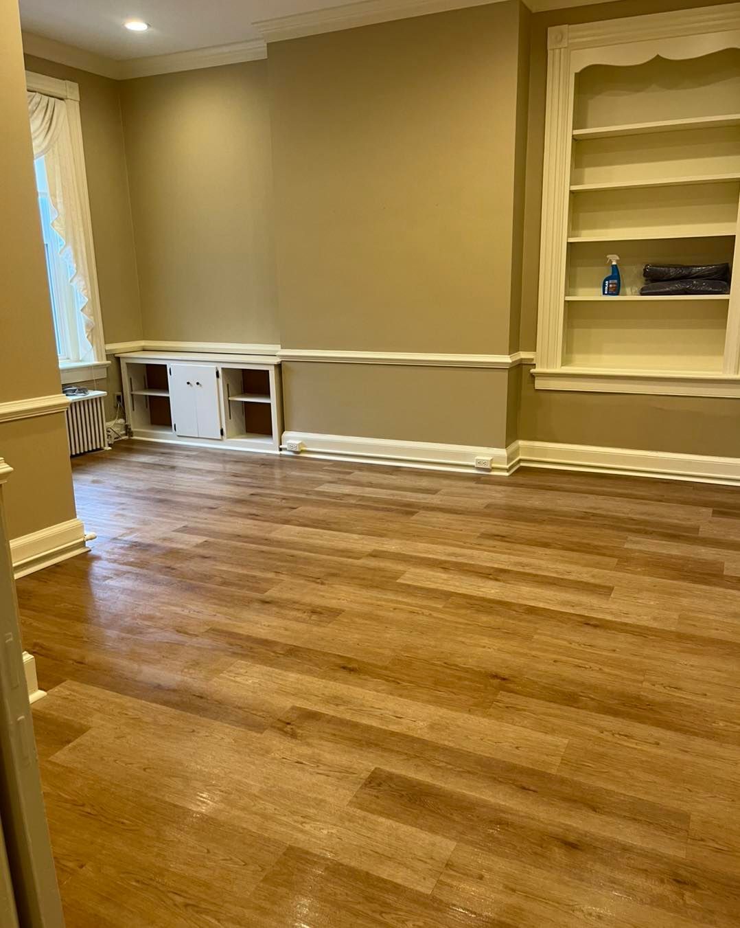 Empty room with wood floors, tan walls, and built-in white cabinets and shelves.