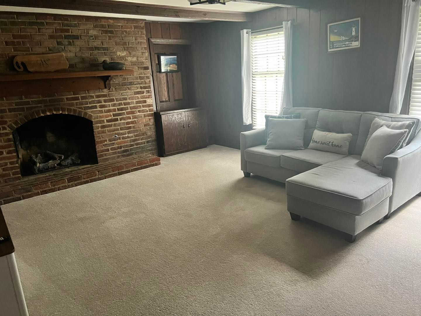 Living room with brick fireplace, gray sectional sofa, and beige carpet.