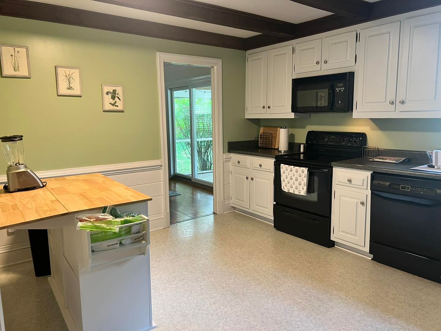 Kitchen with white cabinets, black appliances, green walls, and a wooden island.