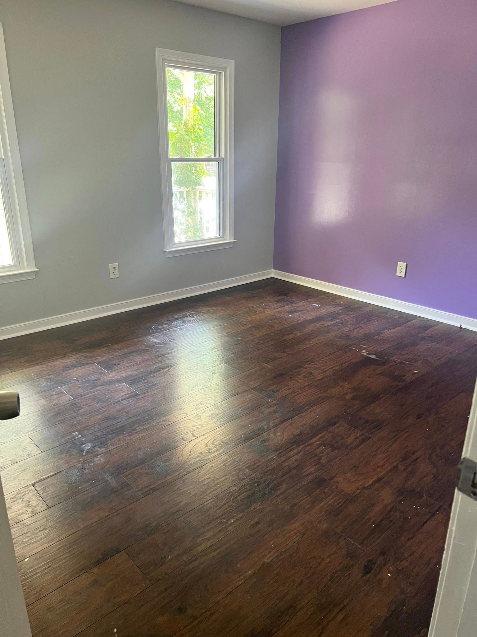 Empty bedroom with purple and gray walls, hardwood floors, and a window.