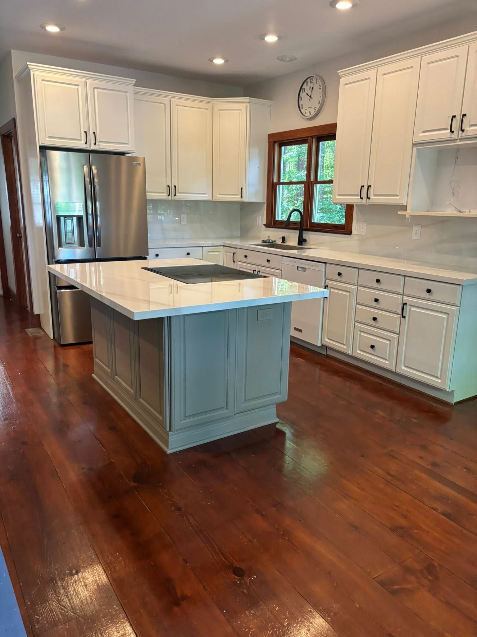 Bright kitchen with white cabinets, an island, and wood floors. Stainless steel refrigerator.