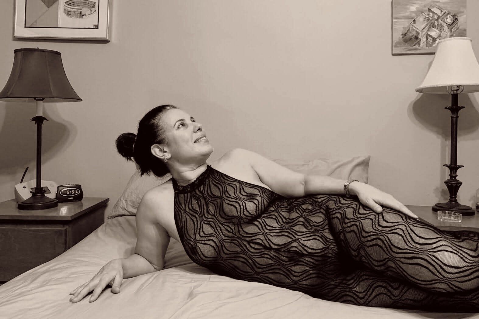 A woman in a black lace bodysuit is lying on a bed.