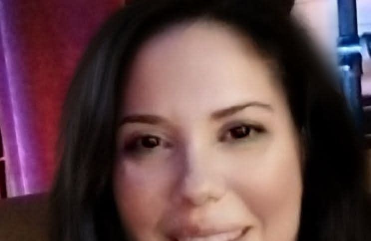 Woman with dark hair and brown eyes smiling.