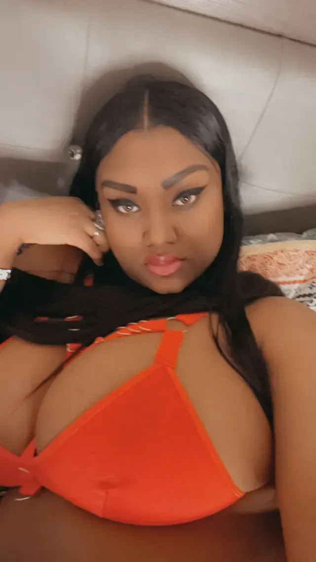 Woman in orange bikini, looking directly at the camera with a serious expression. Black hair, indoor setting.