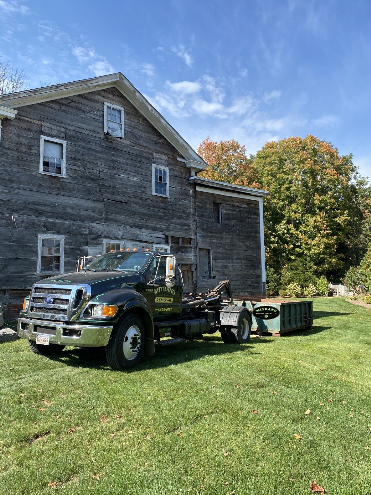 Black work truck with utility trailer parked beside a gray house on a sunny lawn