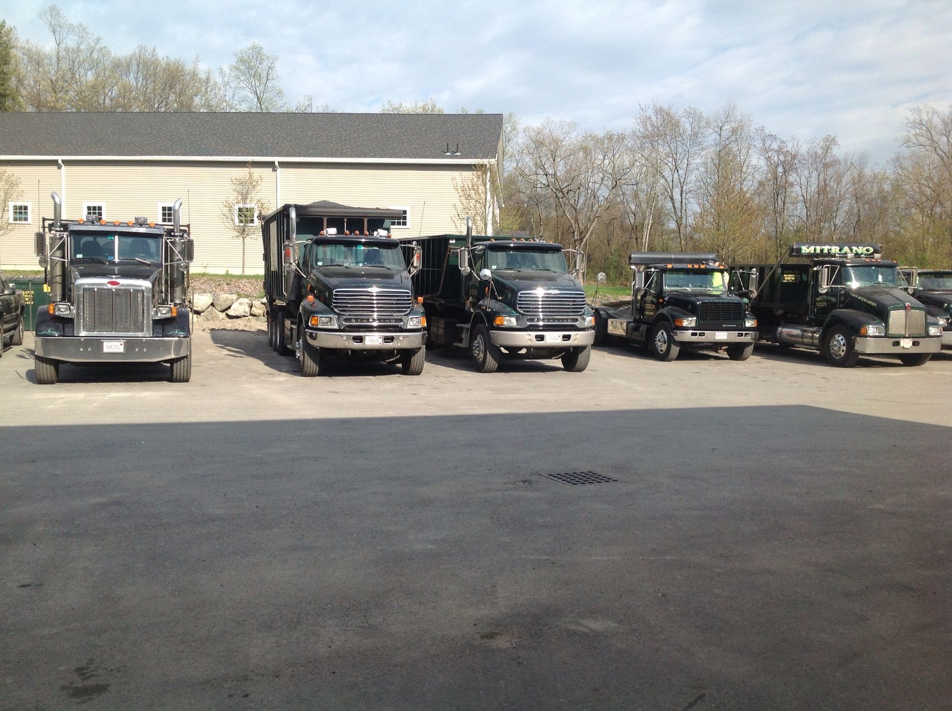 Five black trucks parked in a row outside a beige garage