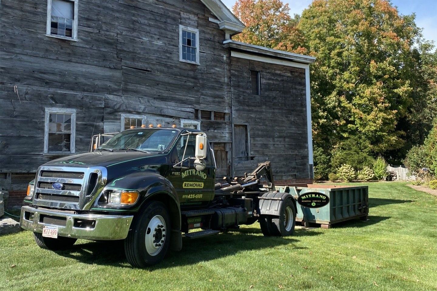 Black work truck with utility trailer parked beside a gray house on a sunny lawn