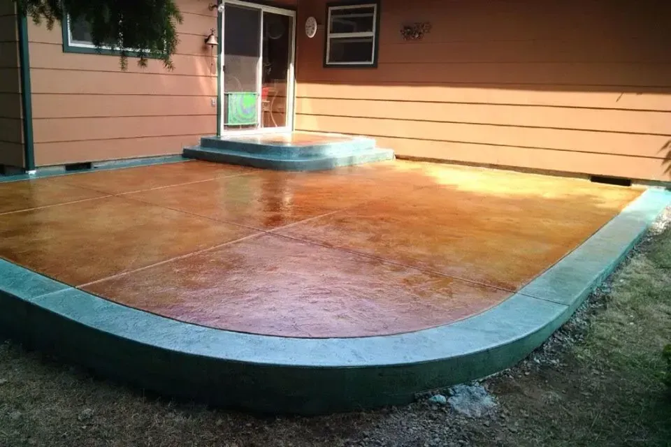 A stained concrete patio with a curved edge, in front of a house with a door.