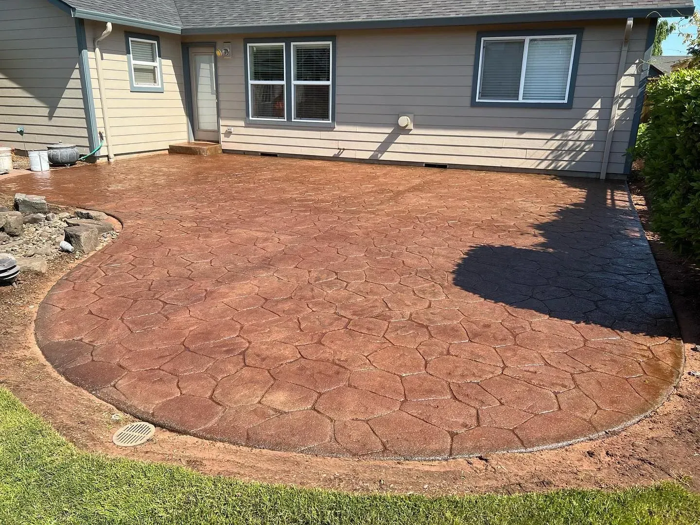 Red stamped concrete patio outside a tan house with green grass border.
