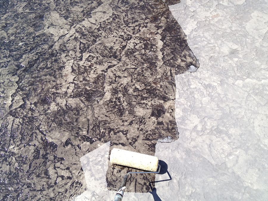 Roller applying dark sealant to concrete, showing contrast between treated and untreated areas.
