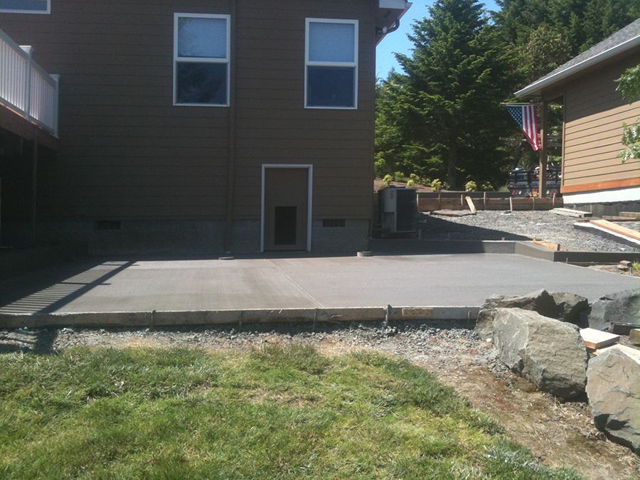 Newly poured concrete patio next to a brown house with a door and windows.
