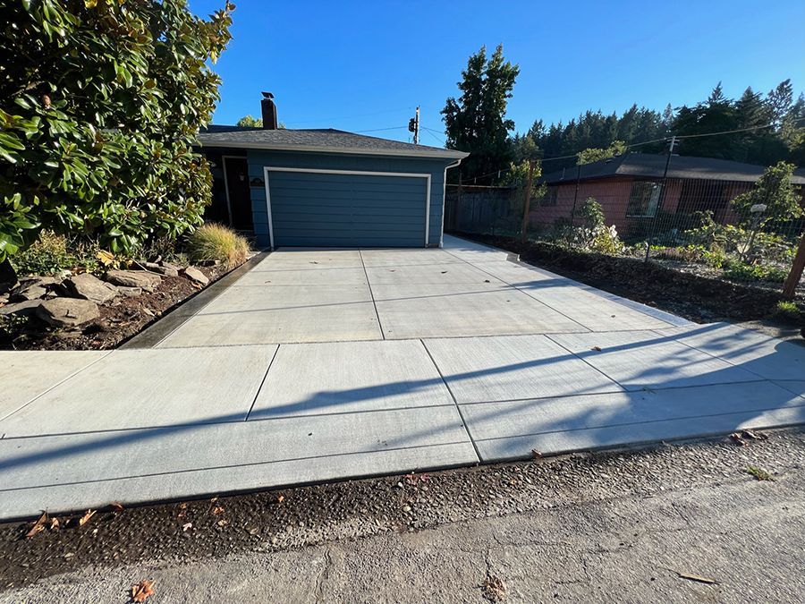 Concrete driveway and sidewalk leading to a blue garage door, bordered by landscaping under a blue sky.