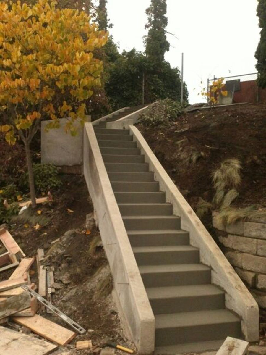 Concrete staircase ascending a hillside with concrete side rails. Yellow tree and greenery surround.