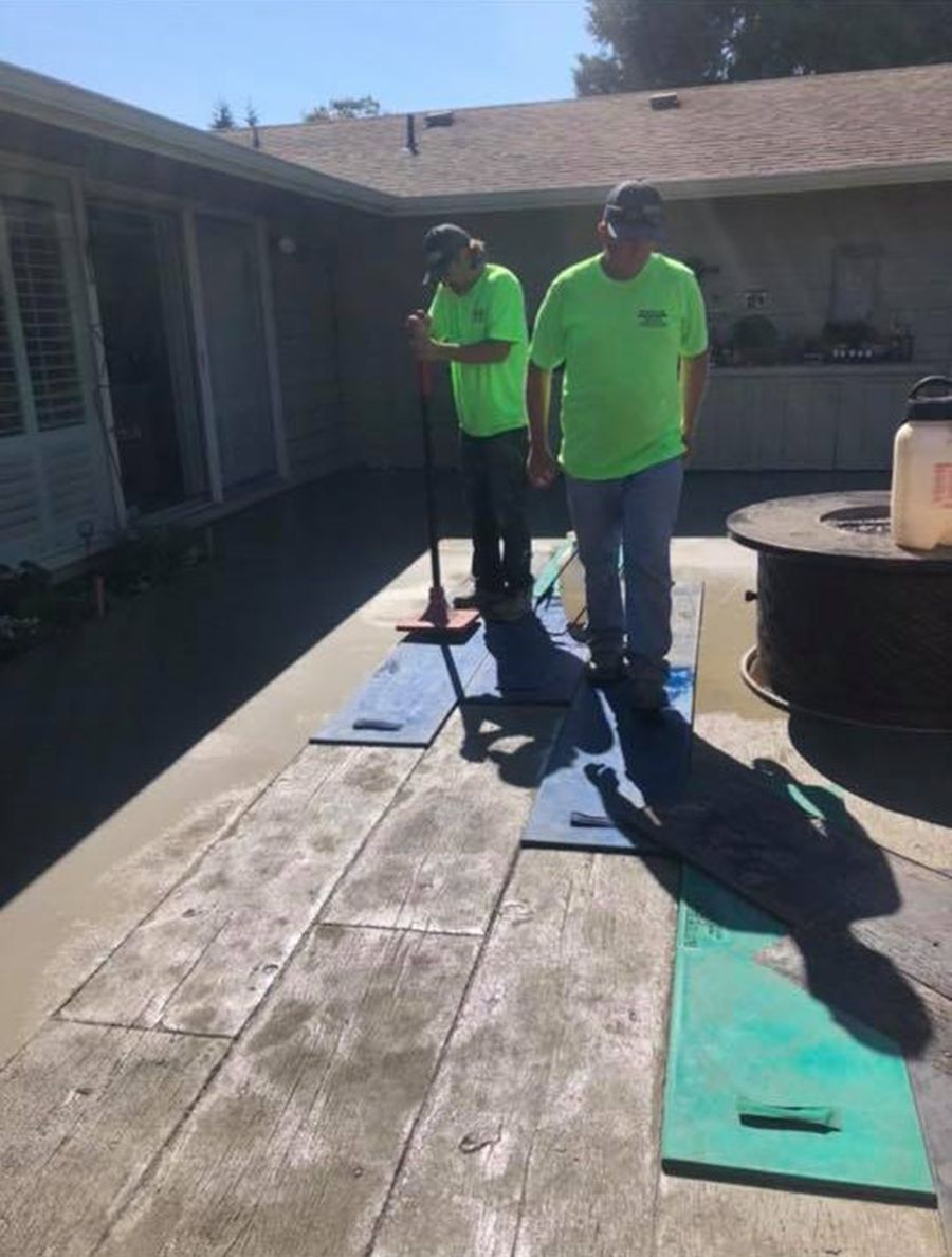 Two people in neon green shirts smoothing concrete patio, using blue and green mats.