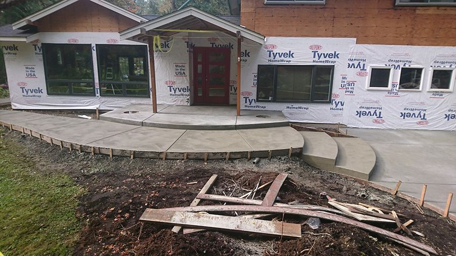 House exterior under construction with newly poured concrete walkway and steps.