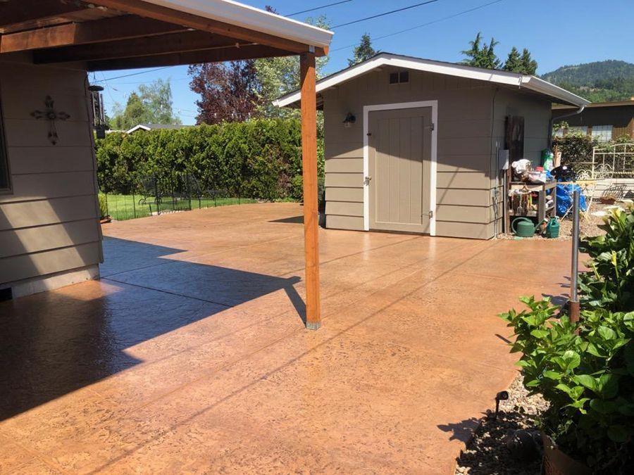 Outdoor concrete patio with shed and pergola, shaded by a wooden beam.