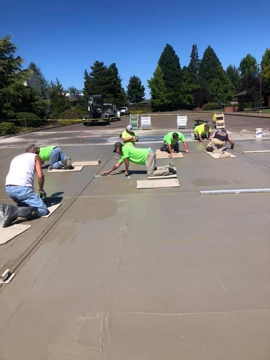Construction workers kneeling and smoothing wet concrete on a sunny day.