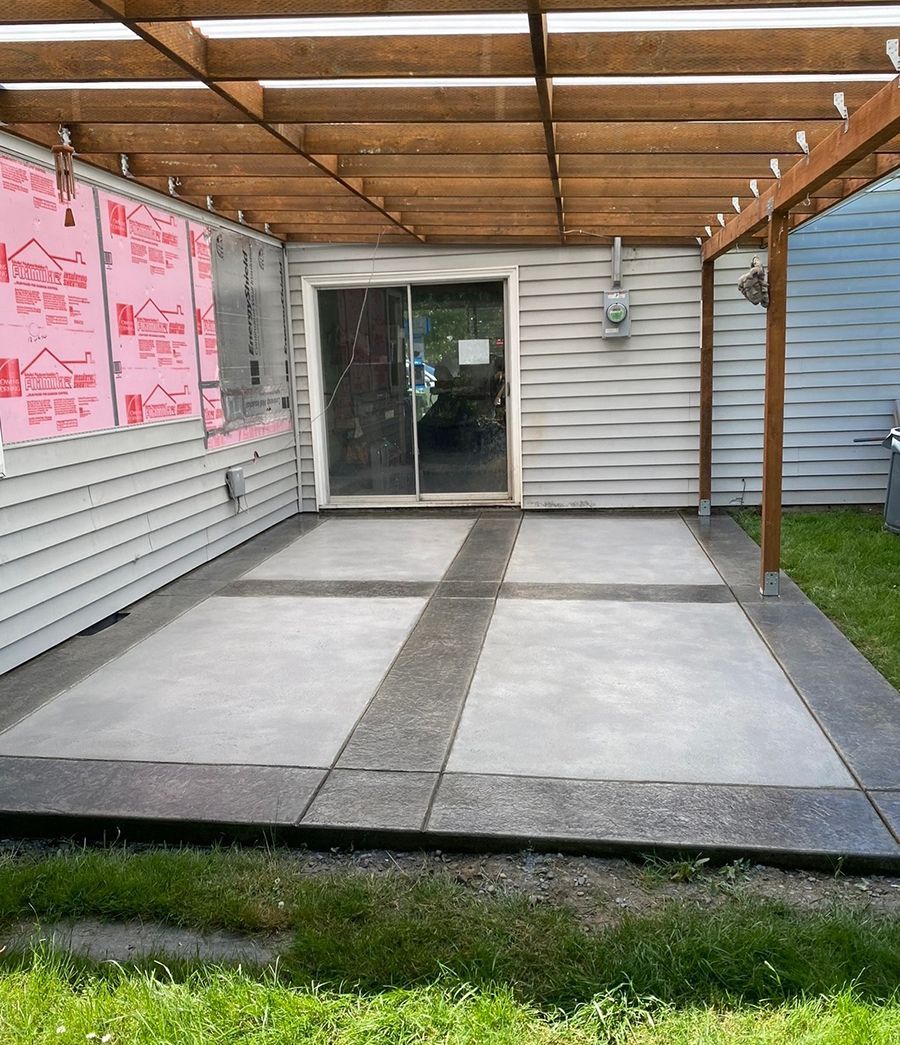 Covered concrete patio with sliding door, gray siding, and wooden pergola.