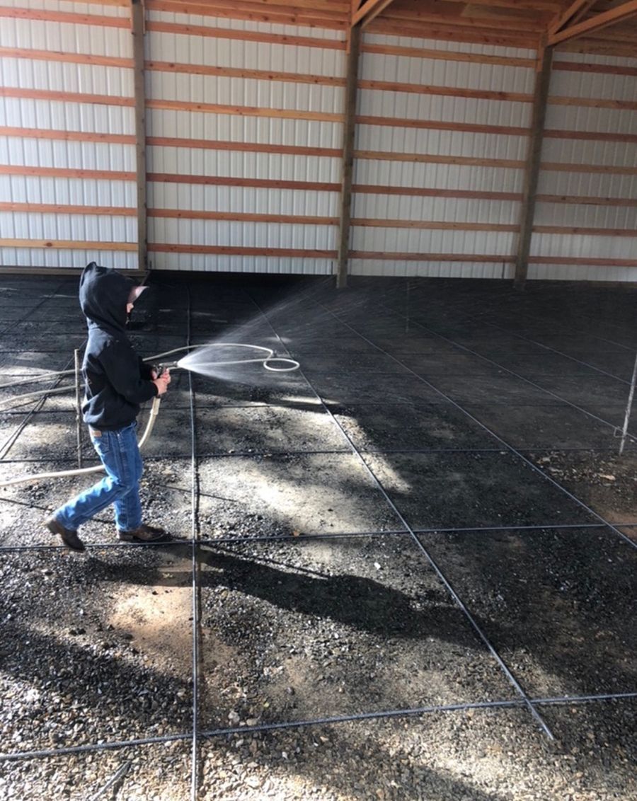 A person sprays water on a concrete floor grid inside a barn.
