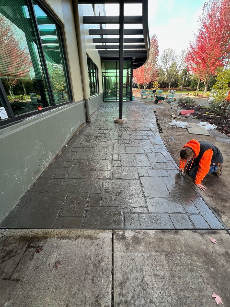 Person kneels, working on a newly paved walkway outside a building.