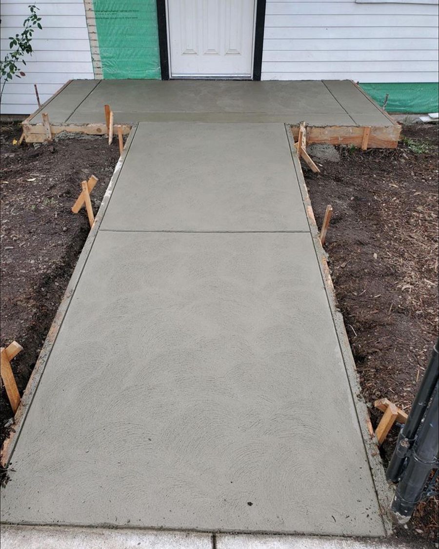 Concrete pathway and landing leading to a white door, framed by wooden forms, in an outdoor setting.