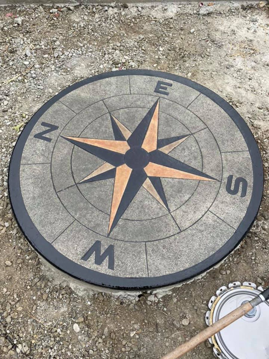 Round concrete compass design, black and orange accents, set in the ground.
