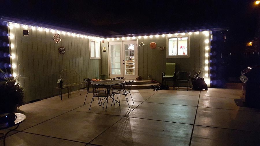 Patio at night with string lights. Door, windows, table, chairs, plants.