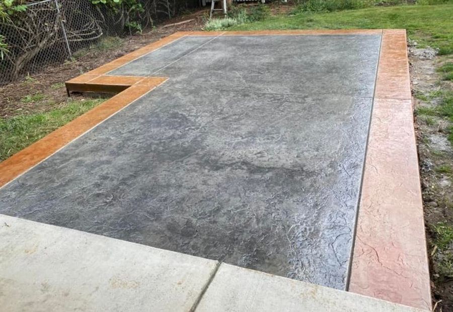 Gray textured concrete patio with brown border, on a grassy lawn.