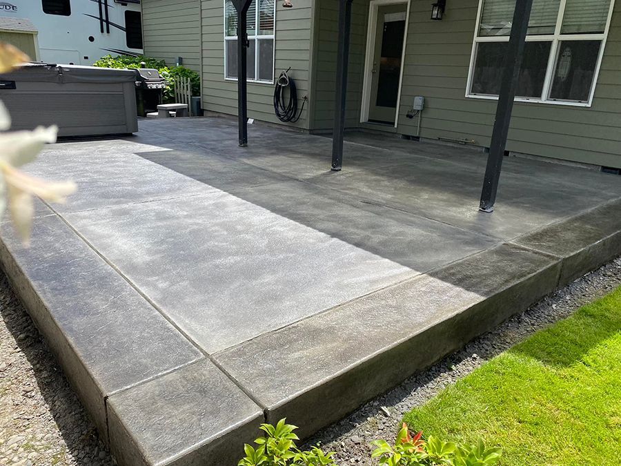 Concrete patio with dark trim, grass, and a house in the background.