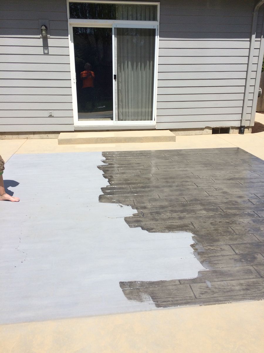 A patio being painted light gray. Half the concrete is finished, showing a brick pattern.