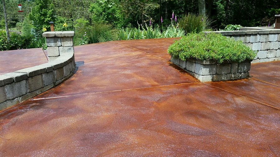 A weathered, reddish-brown concrete patio with gray stone retaining walls; a green bush sits in one wall.