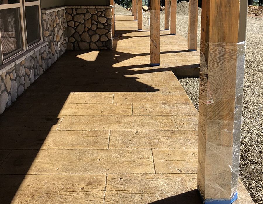 Stained concrete porch with stamped wood plank pattern, columns, and stone wall.