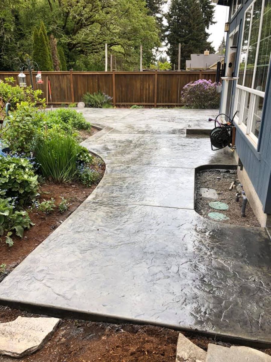 Gray stamped concrete patio with garden beds and wooden fence.