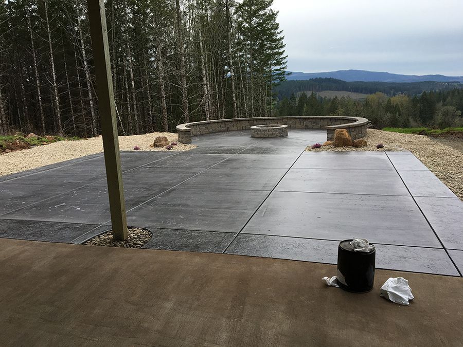 Concrete patio with fire pit, forest and mountain view. Gravel border, overcast sky.