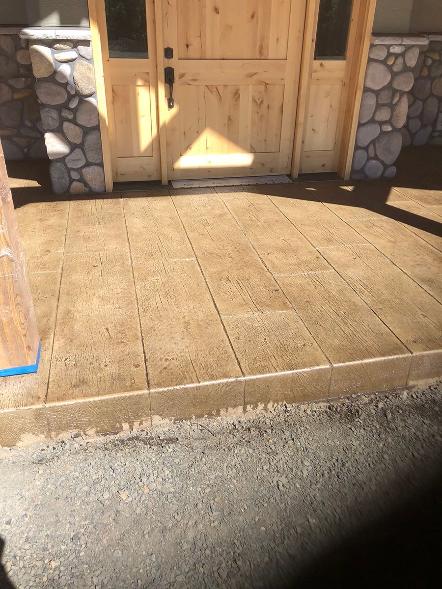Wooden front door with a stamped concrete porch in a tan color. Stone accents and blue tape visible.