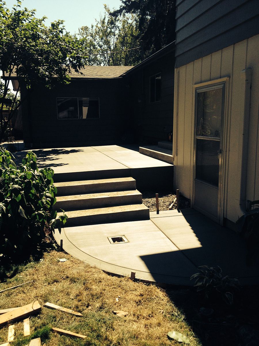 Newly poured concrete patio and stairs leading to a dark building. Green grass surrounds.