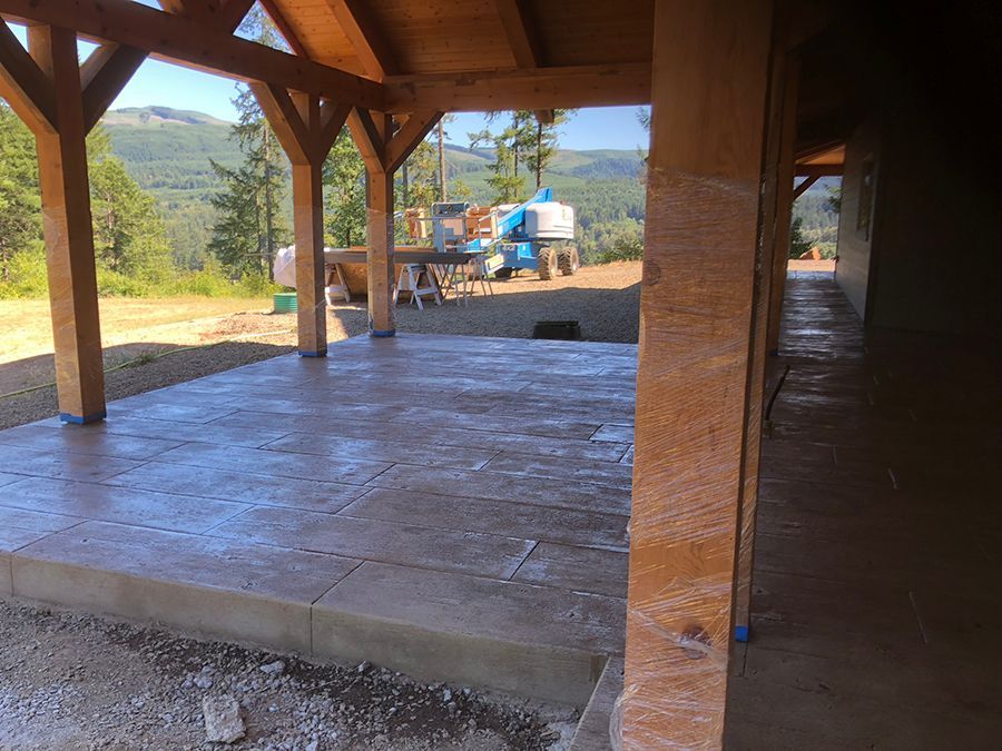Covered outdoor patio with freshly poured concrete floor and wooden support beams, mountain view in the background.