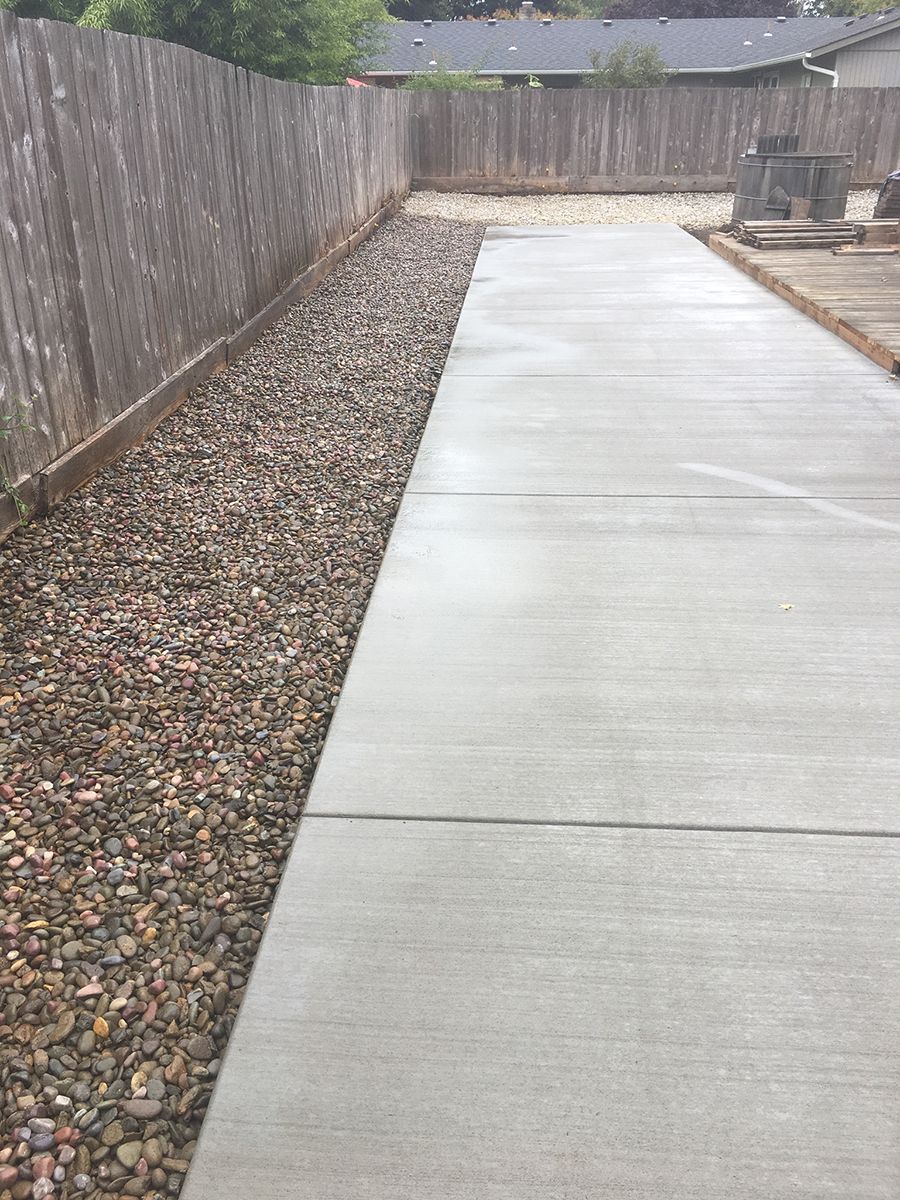 A concrete walkway bordered by gravel next to a wooden fence.