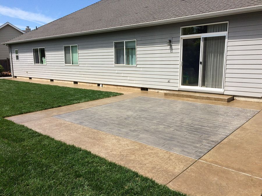 Gray house exterior with sliding door and a paved patio area next to green grass.