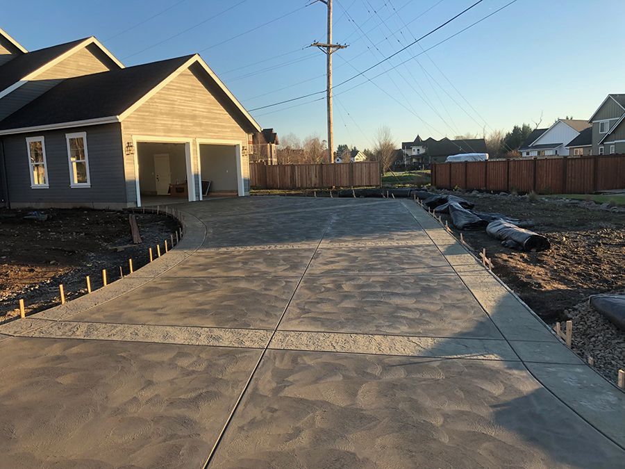 Newly poured concrete driveway leading to a two-car garage of a house. The sky is blue.