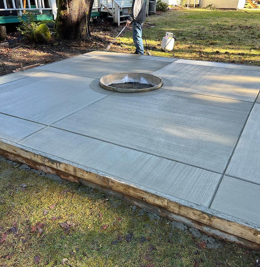 Newly poured concrete patio with a fire pit, being finished by a person in blue jeans.