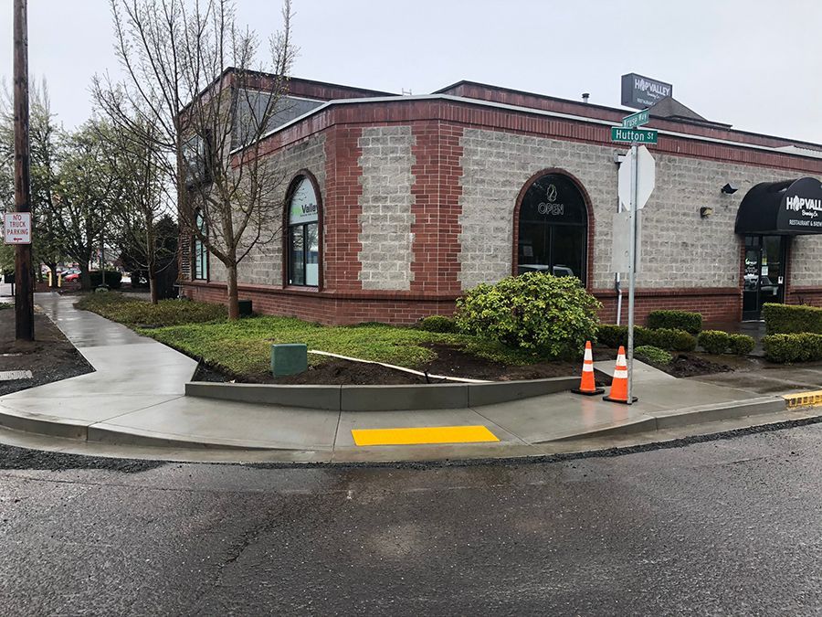 Corner of a building with a sidewalk, curb ramp, and safety cones.
